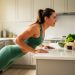 Woman in activewear doing a supported push-up with her hands on a kitchen counter, with healthy items and resistance bands in a tidy background.